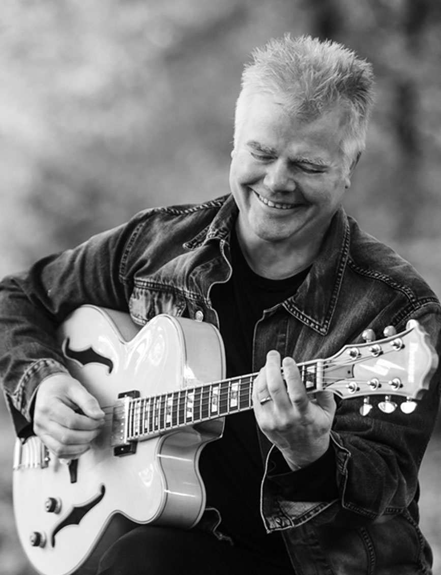 Ian Raba playing hollowbody guitar, autumn forest setting